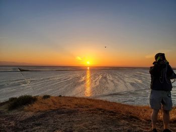 Rear view of people standing on beach during sunset