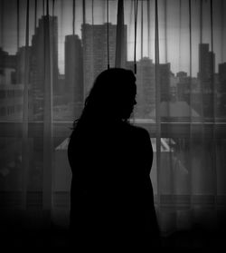 Silhouette woman standing by curtain at home