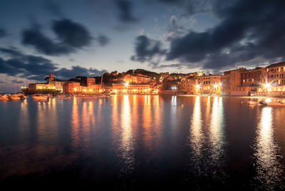 Illuminated city by sea against sky