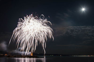 Firework display over sea against sky at night