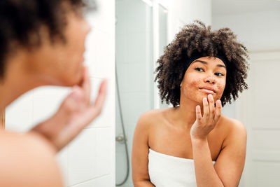 Teenage girl applying face powder reflecting on mirror in bathroom
