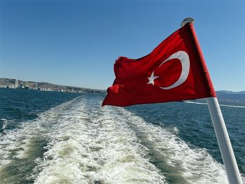 Red flag on sea against clear blue sky