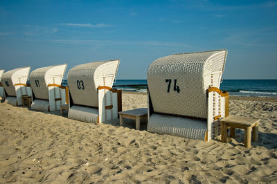 Hooded chairs on beach against sky