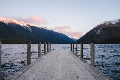 Wooden pier on lake by snowcapped mountains against sky