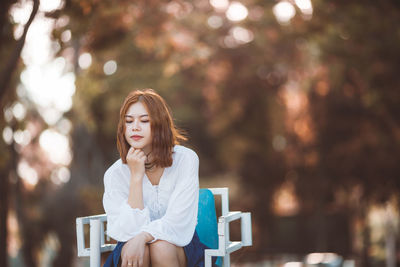 Thoughtful young woman sitting on chair against trees at park