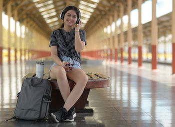 A teenage european woman sits and listens to music while waiting for a train to travel.