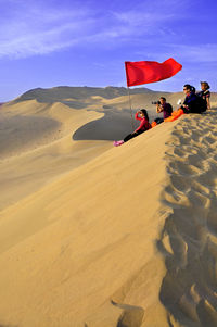 People sitting by red flag at desert against sky