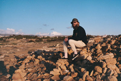 Man in sunglasses sitting on stones against blue sky