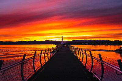 Pier over sea against orange sky