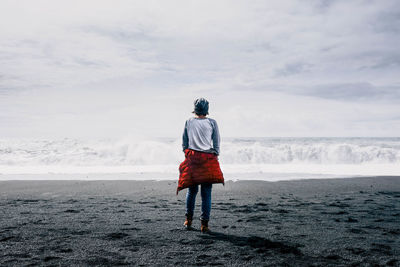 Rear view of man standing on beach against sky