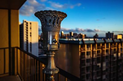 Close-up of old brass light fixture with metal railing against buildings