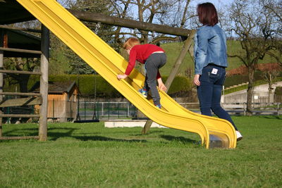 Side view of mother looking at son climbing slide at playground