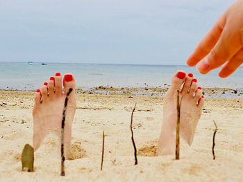 Cropped hand reaching legs at beach