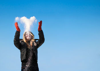 Happy young woman throwing snow against clear blue sky