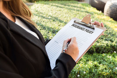 Midsection of female agent with insurance documents in yard