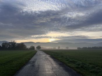 Empty road amidst field against sky during sunset