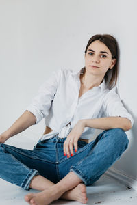 Portrait of young woman sitting against wall