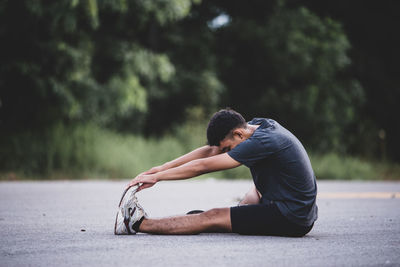 Side view of young man sitting on road
