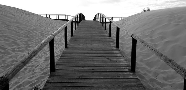 Wooden footbridge on pier by sea against sky