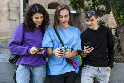 Friends using mobile phone while standing outdoors on the street.