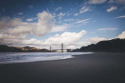 View of suspension bridge over sea against cloudy sky