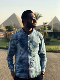 Young man wearing sunglasses standing against built structure