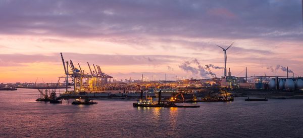 Cranes at commercial dock against sky during sunset