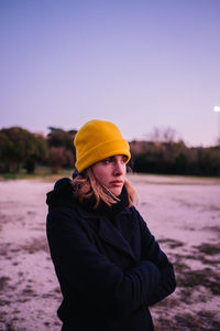 Young woman wearing hat standing in snow against sky