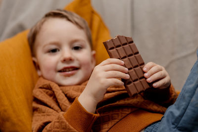 Little adorable boy sitting on the couch at home and eating chocolate bar. child and sweets