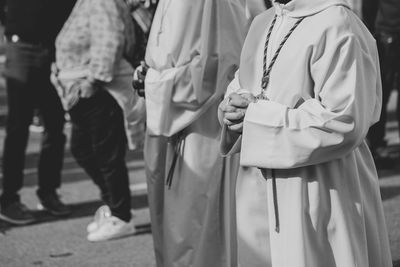 Midsection of women praying while standing on road by people in city