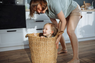 Mom rolls her daughter on the floor in a wicker basket