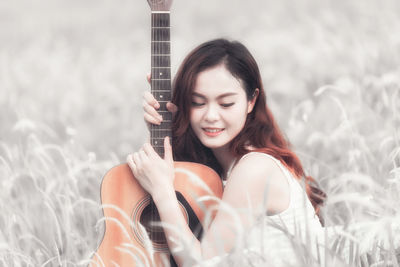 Side view of young woman with guitar on field