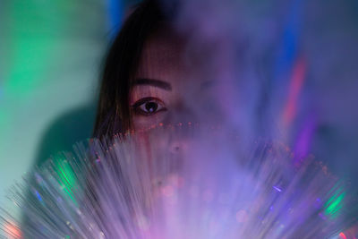 Close-up portrait of young woman holding illuminated fiber optic in darkroom
