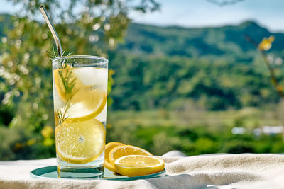 Summer refreshing lemonade drink or alcoholic cocktail with ice, rosemary and lemon slices on table