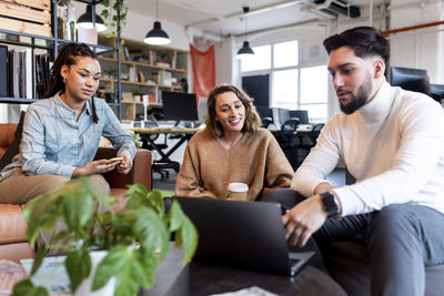 Young businessman with laptop explaining to colleagues in office