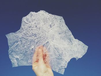 Close-up of hand on snow against blue sky