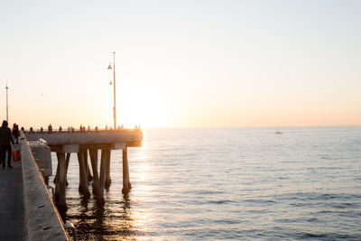 Scenic view of people standing on pier by sea against clear sky during sunset