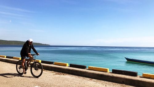 Woman on bicycle by sea against sky