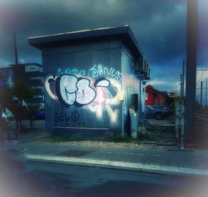 Graffiti on wall by road against sky in city