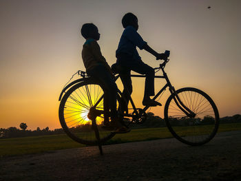 Silhouette people riding bicycle against sky during sunset