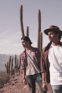 Young men looking away while standing against cactus on field