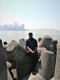 Man sitting on rock by sea against clear sky