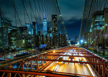 Illuminated bridge and buildings against sky at night