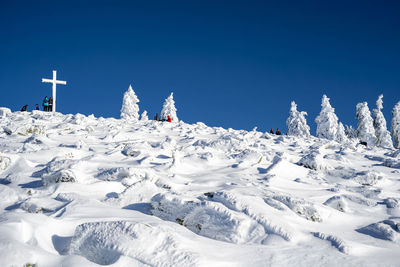 Low angle view of people on snow covered land against clear blue sky