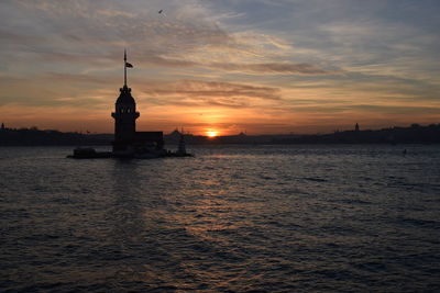 Silhouette building by sea against sky during sunset