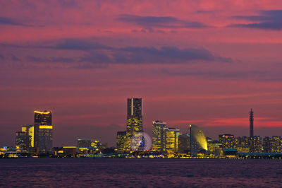 Illuminated buildings by sea against sky during sunset