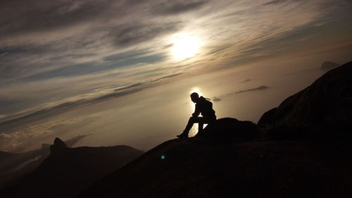 Silhouette man standing on rock against sky during sunset