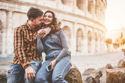 Young couple embracing while sitting against historical building