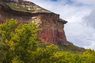 Low angle view of rocks on mountain against cloudy sky