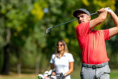 Golfing couple at a tee box, enjoying a game of golf on a beautiful sunny day, man hitting a ball